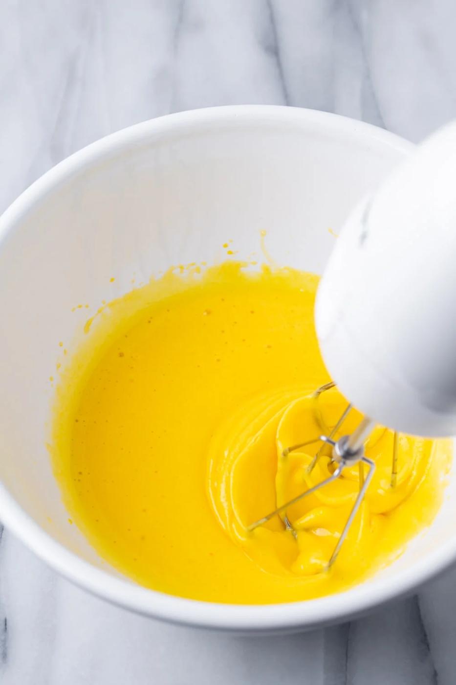 Egg yolks in a white bowl being beat with a white beater to make the batter for a guava swiss roll