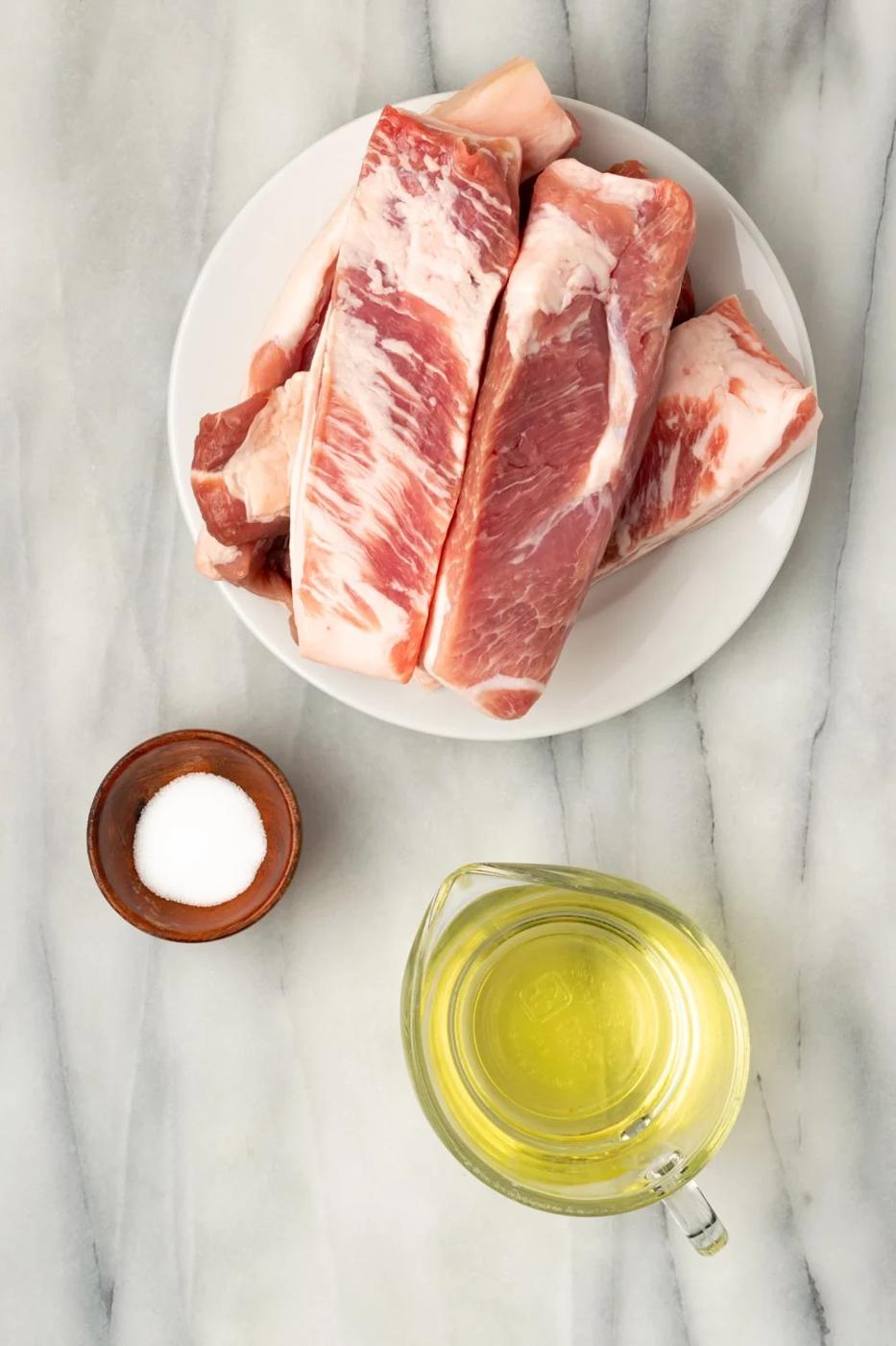 Ingredients for chicharrones de puerco on plates or bowls: pork belly, vegetable oil, salt.