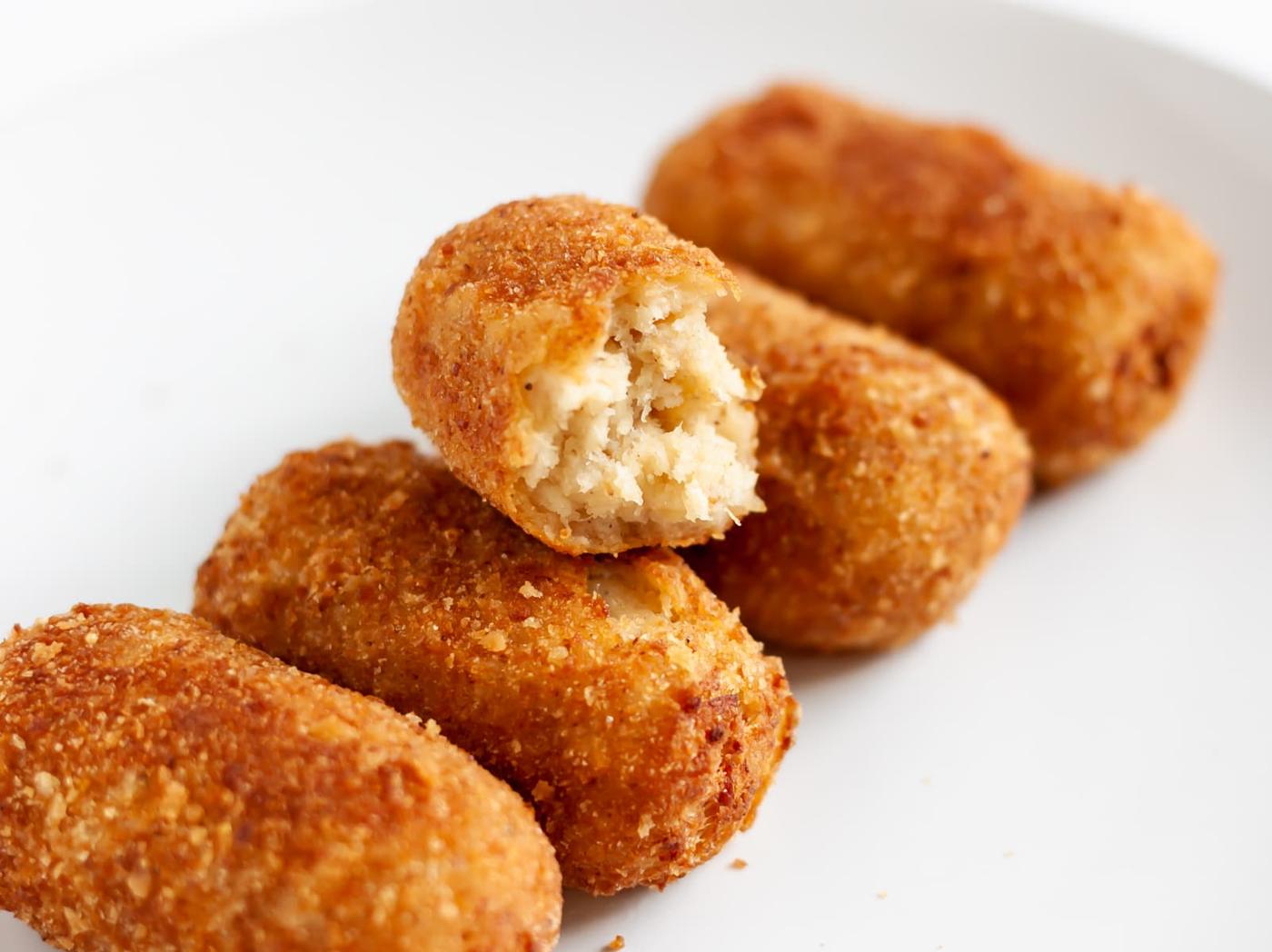 chicken croquettes on a white plate with a bitten one
