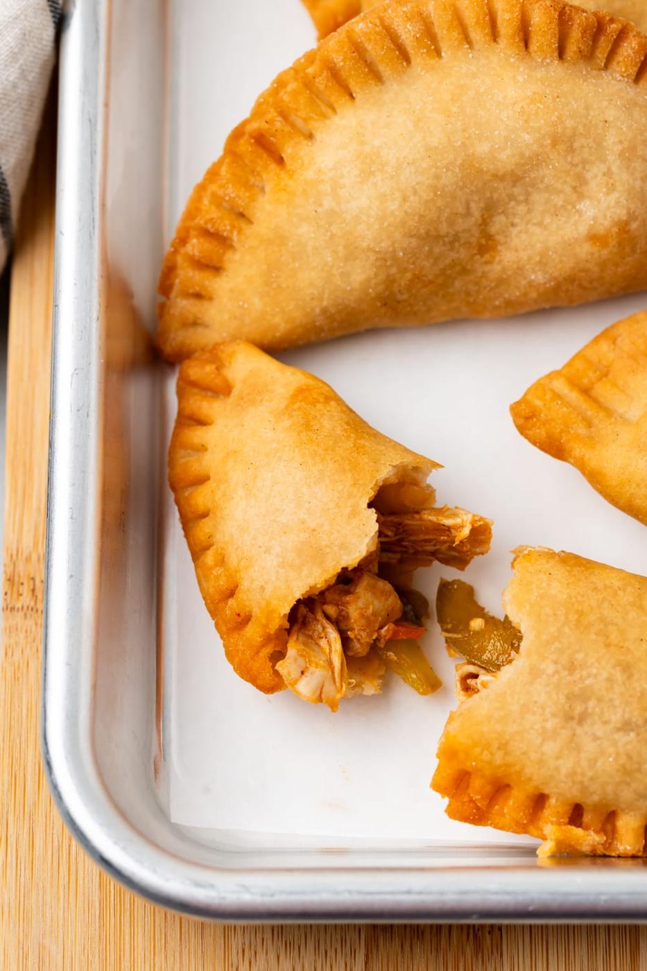 A Chicken Empanada on a parchment lined baking sheet that is broken in half with more empanadas on the background