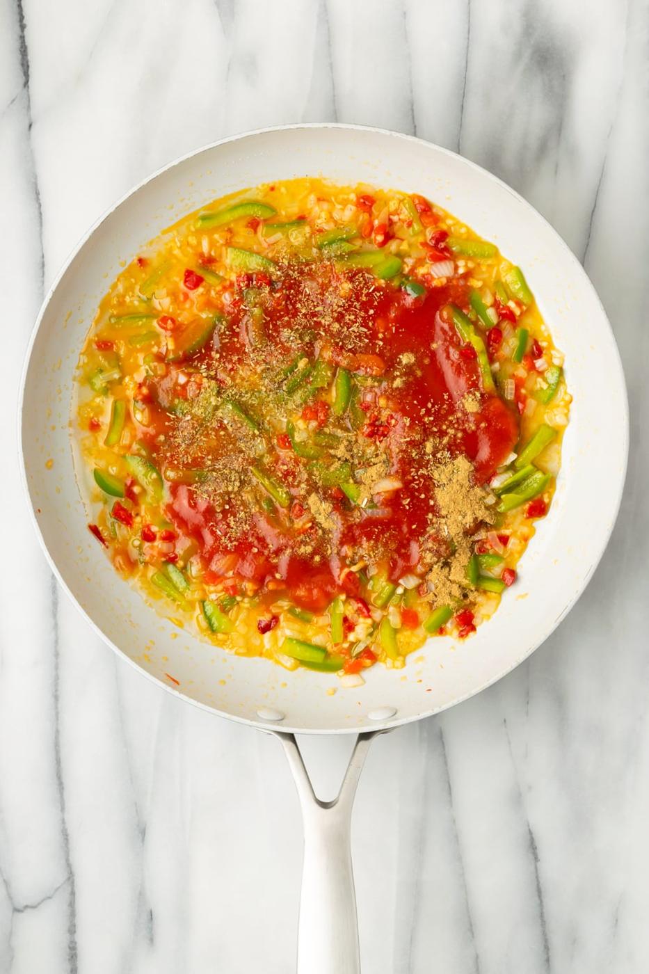 Tomato sauce, dry wine, and spices being added to a sofrito in a pan to make cuban chicken empanada filling on a marble background