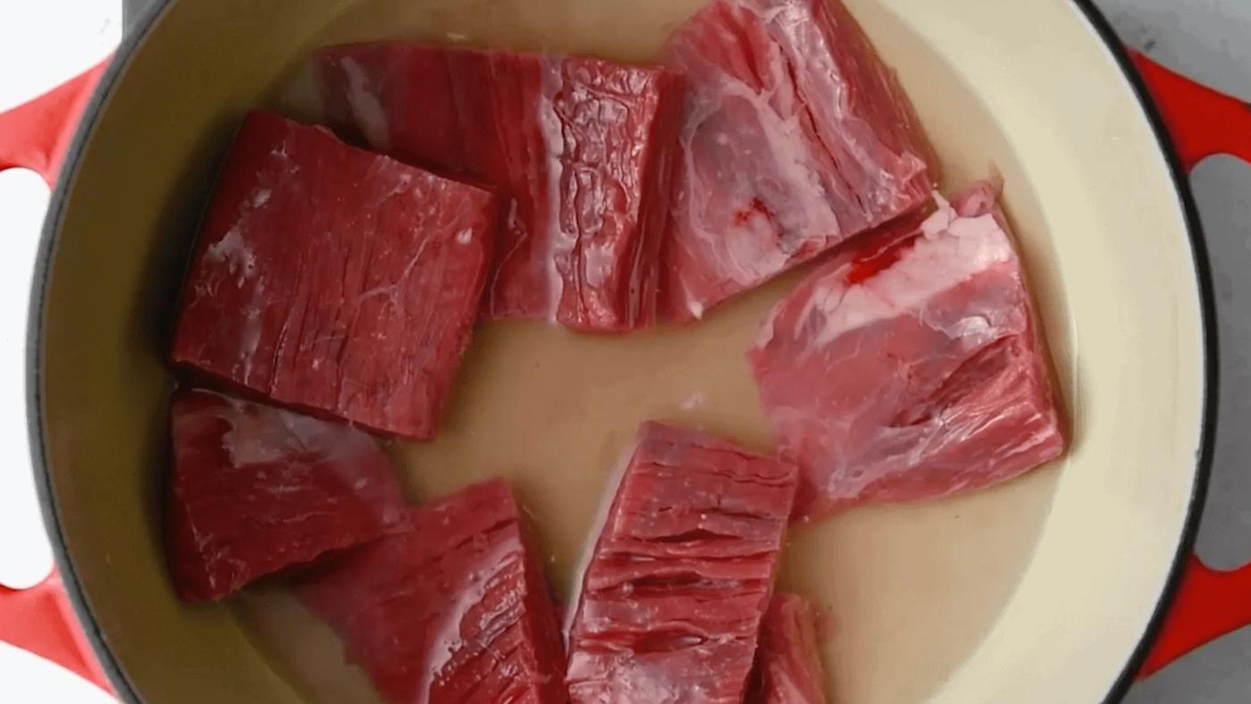 flank steak with water in a Dutch oven ready for cooking