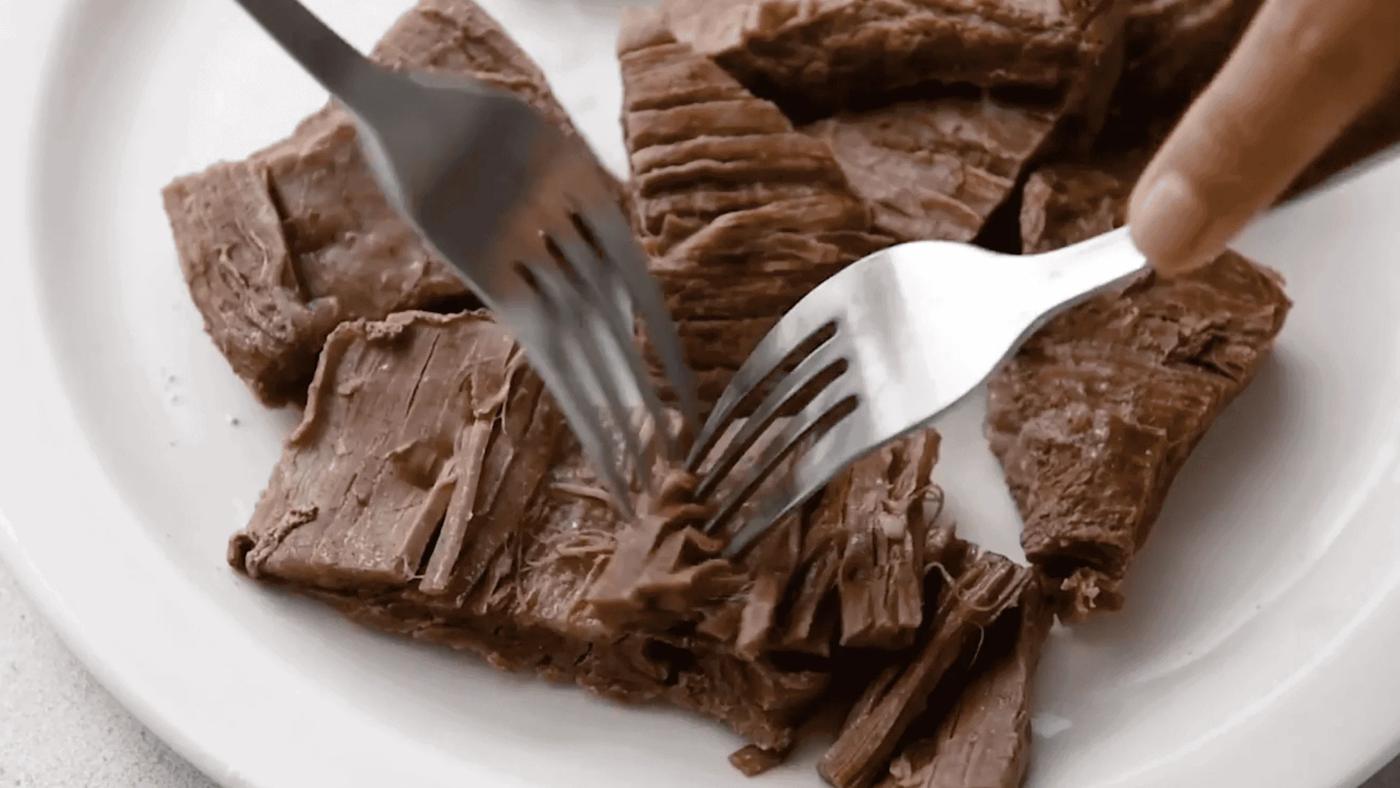 shredding flank steak using two forks on a white plate