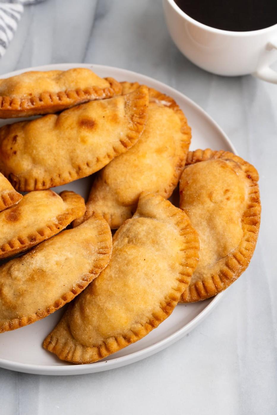 Guava Cream Cheese Empanadas on a white plate with a mug of coffee on the side.