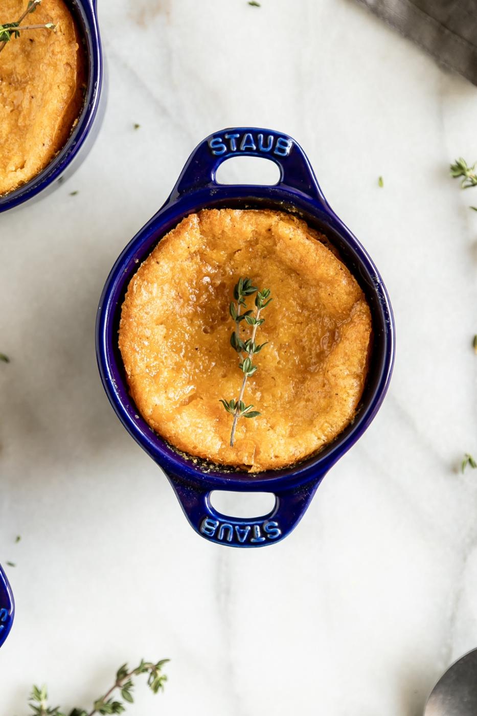 Golden baked cheesecake in a blue Staub ramekin with thyme garnish, perfect for dessert lovers.