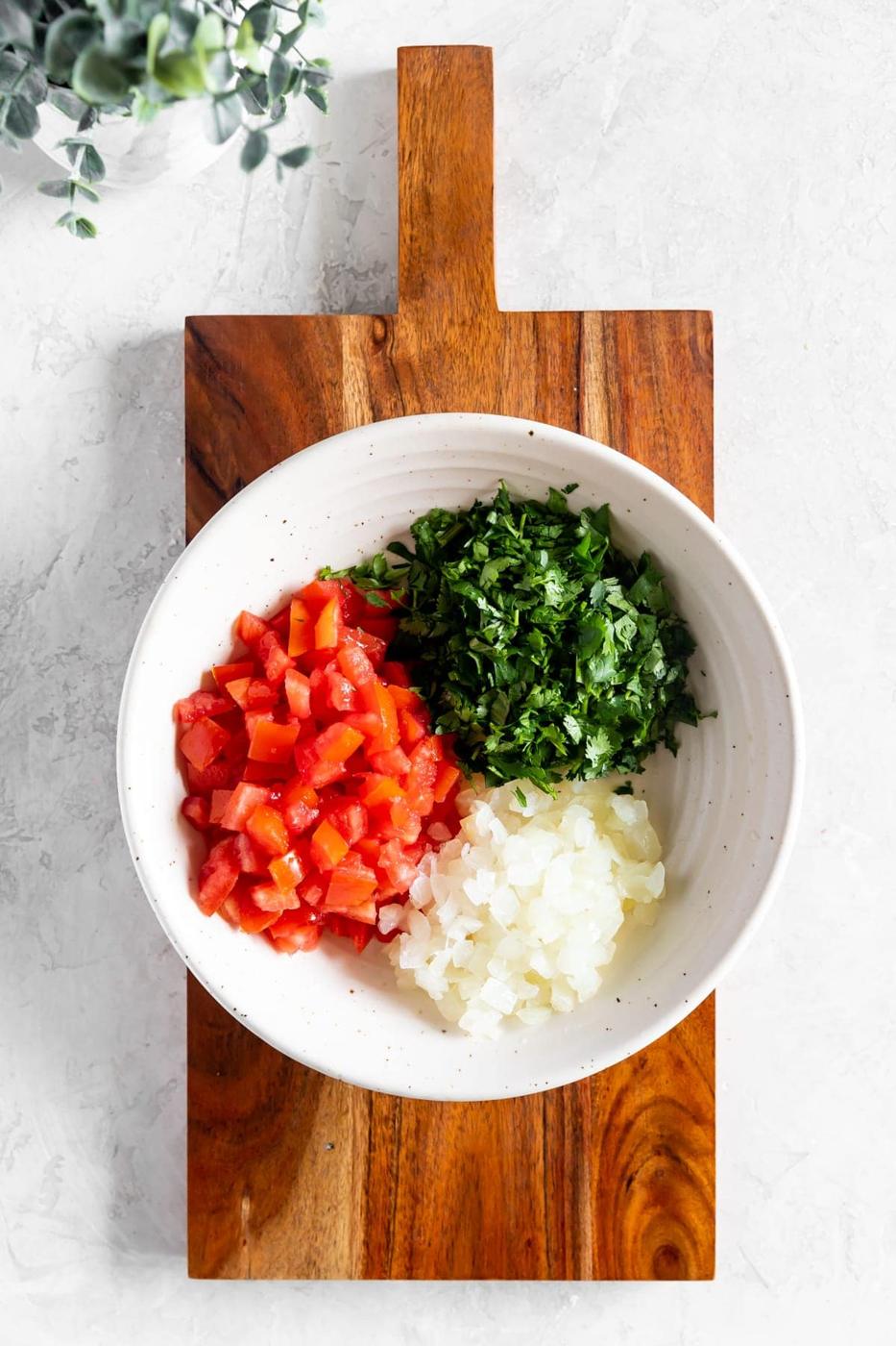 chopped tomatoes, chopped cilantro and chopped onions in a bowl on a wood cutting board