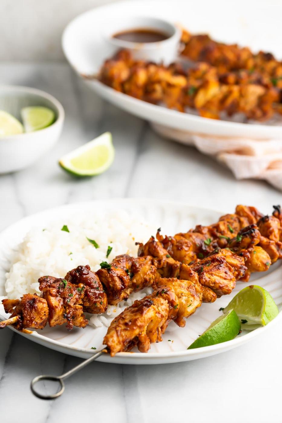 Cuban pinchos de pollo glazed with guava bbq sauce on a white plate with white rice and lime wedges