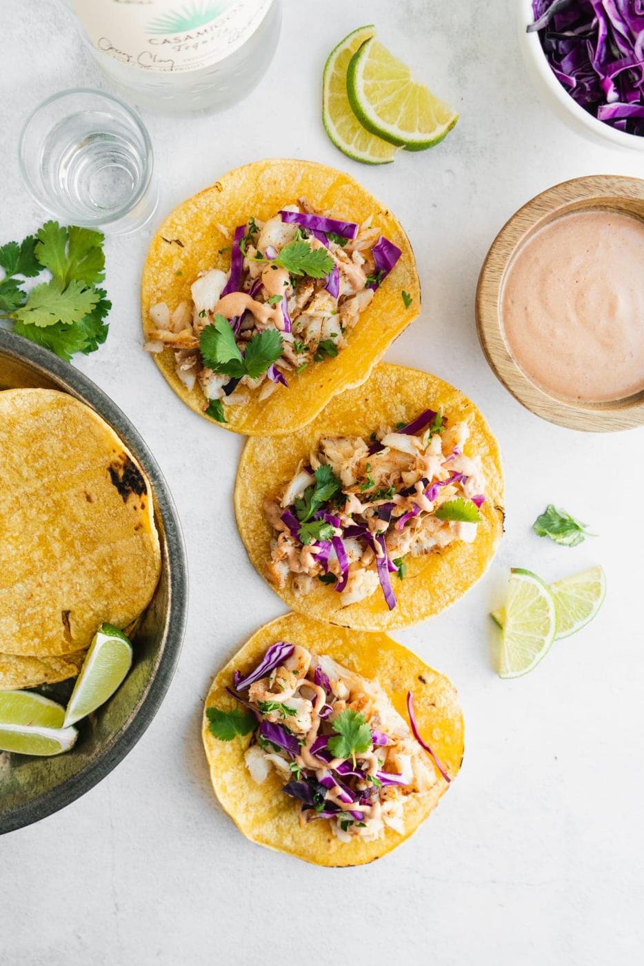 fish tacos on a white table with chipotle mayo and slaw