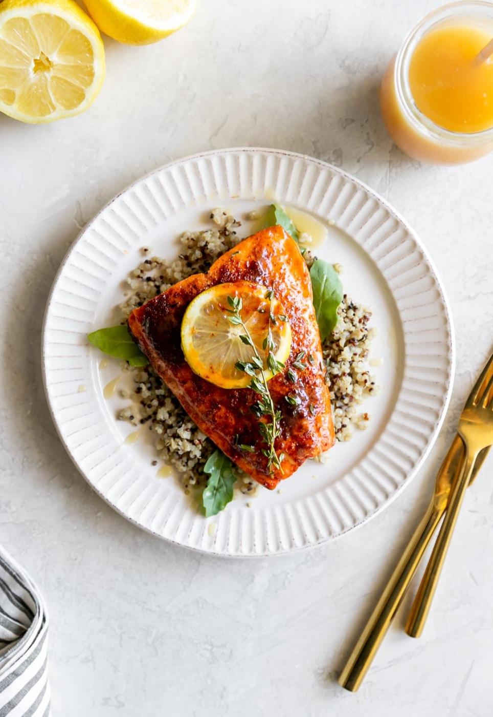 spicy salmon with honey butter on a white plate with a lemon slice and a gold fork and knife