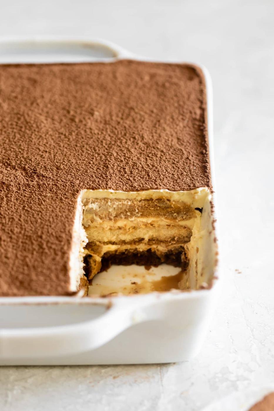 tiramisu with a slice removed to see the filling and layers of mascarpone and espresso soaked ladyfingers