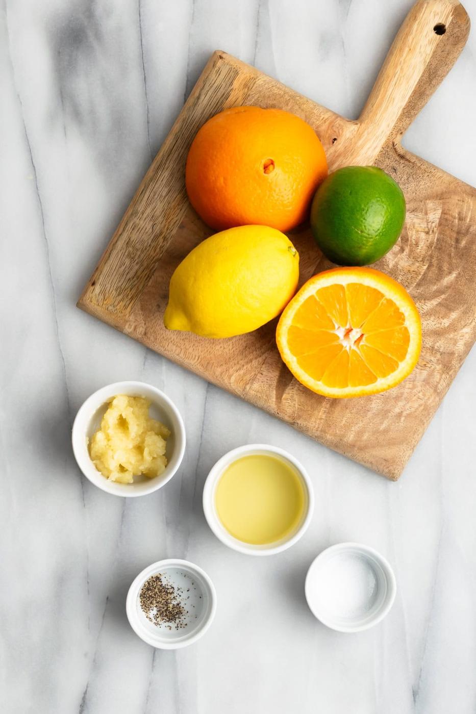 ingredients for garlic mojo dipping sauce - lemon, lime, orange, garlic, oil, salt and pepper on a marble slab
