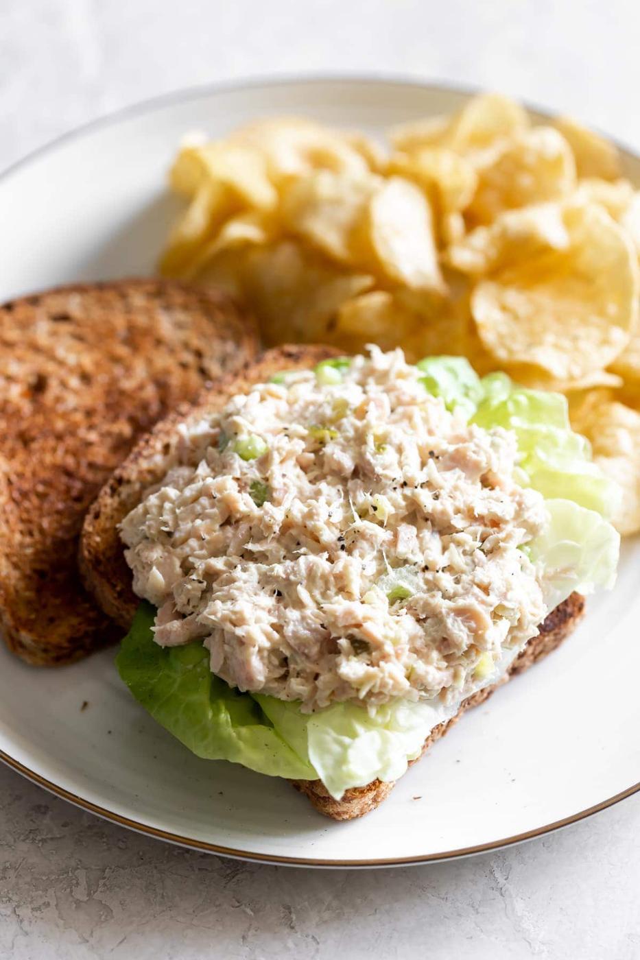 tuna salad sandwich on boston lettuce with chips on a white plate