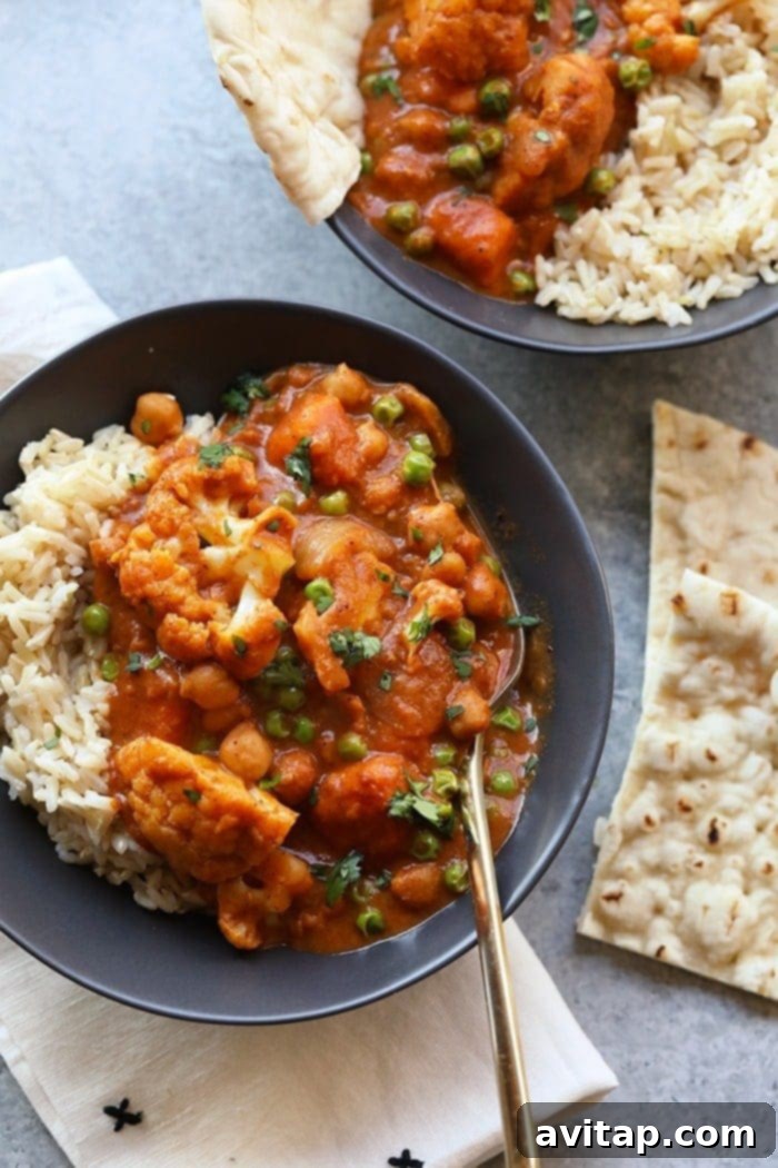 A bowl of vibrant cauliflower tikka masala with fluffy rice and warm naan bread on the side, showcasing a delicious plant-based meal.