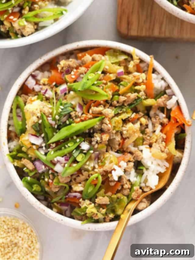 A bowl of vibrant egg roll in a bowl with seasoned ground turkey, shredded cabbage, carrots, and a savory sauce, garnished with green onions.