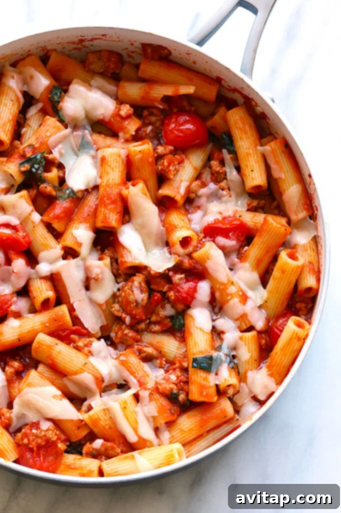 A skillet brimming with delicious 30-minute sausage pizza pasta, topped with melted cheese, bell peppers, and fresh basil, ready to serve.