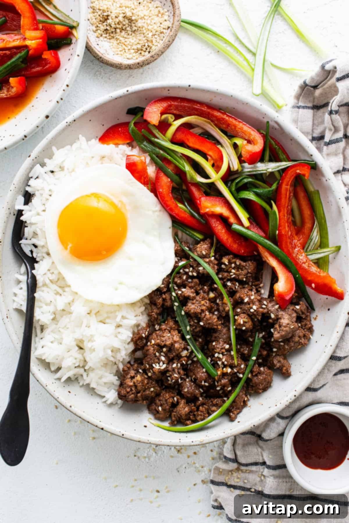 A plate of Korean ground beef served over rice, garnished with green onions, sesame seeds, and a perfectly fried egg, offering a complete and flavorful meal.