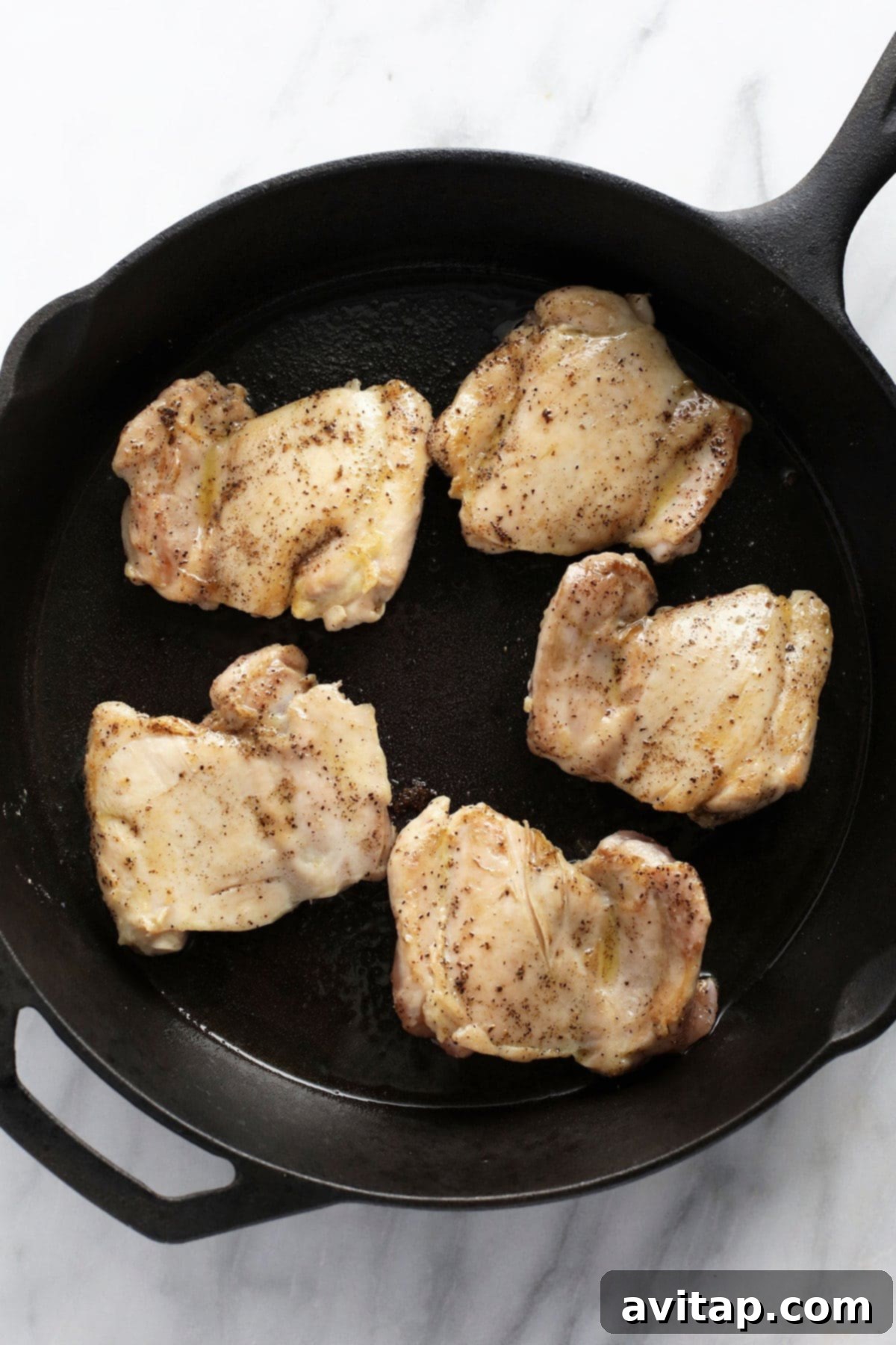 Close-up of boneless, skinless chicken thighs being perfectly seared to a golden brown in a cast iron skillet, crucial for deep flavor.