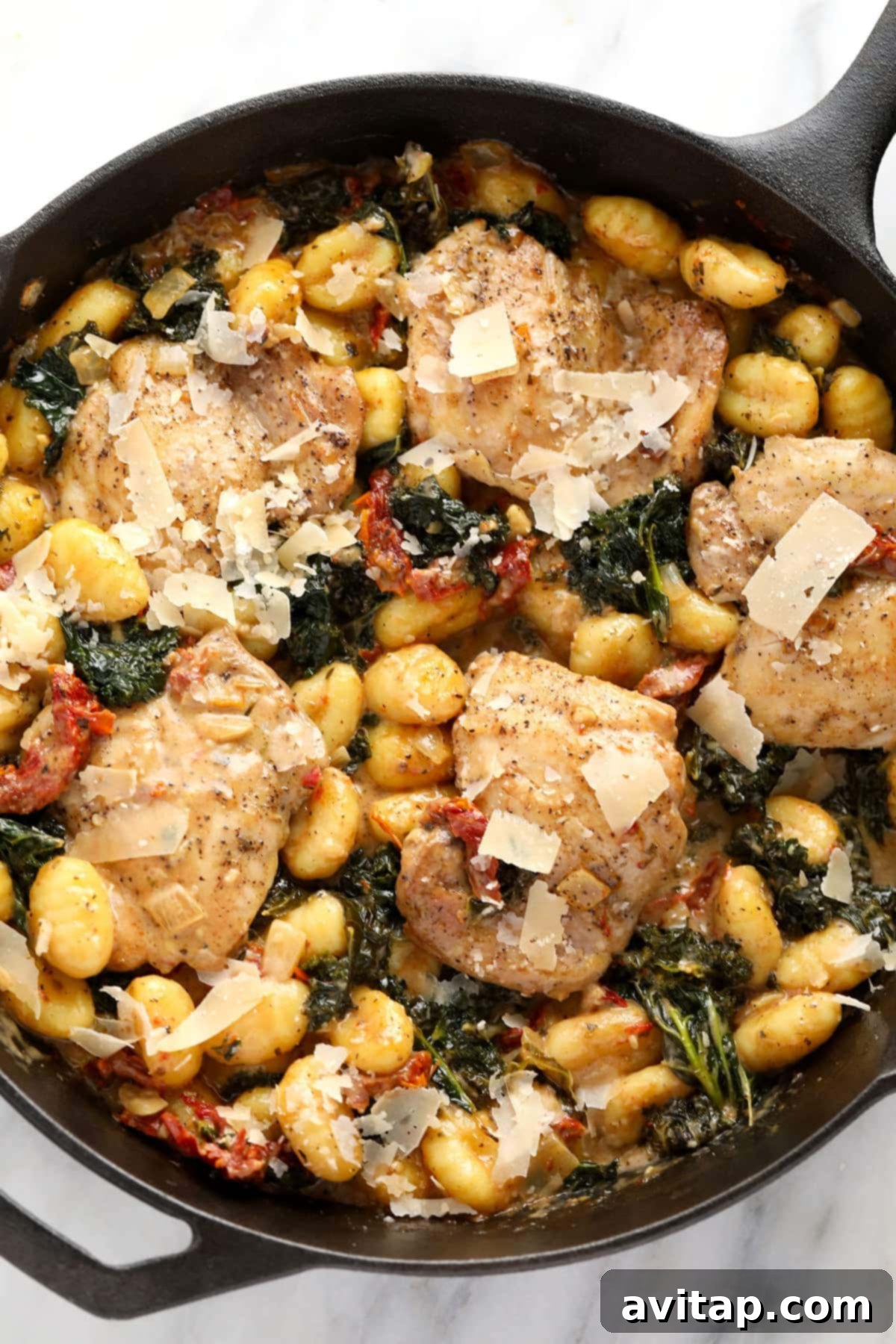A serving of Creamy Tuscan Chicken and Gnocchi generously topped with grated Parmesan cheese, glistening with creamy sauce, ready to be enjoyed.