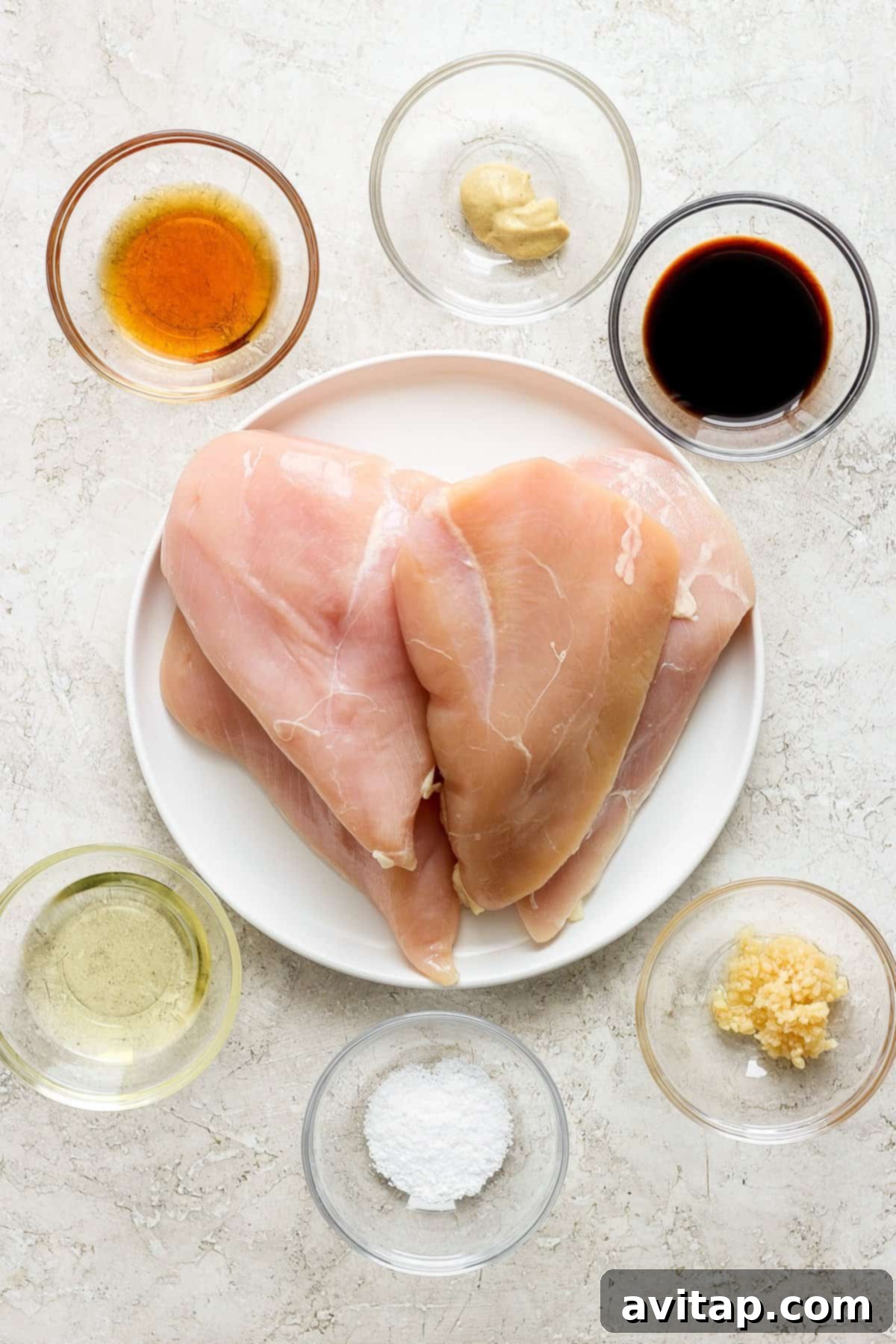 Raw chicken breasts on a plate with various seasonings and marinade ingredients arranged around it.