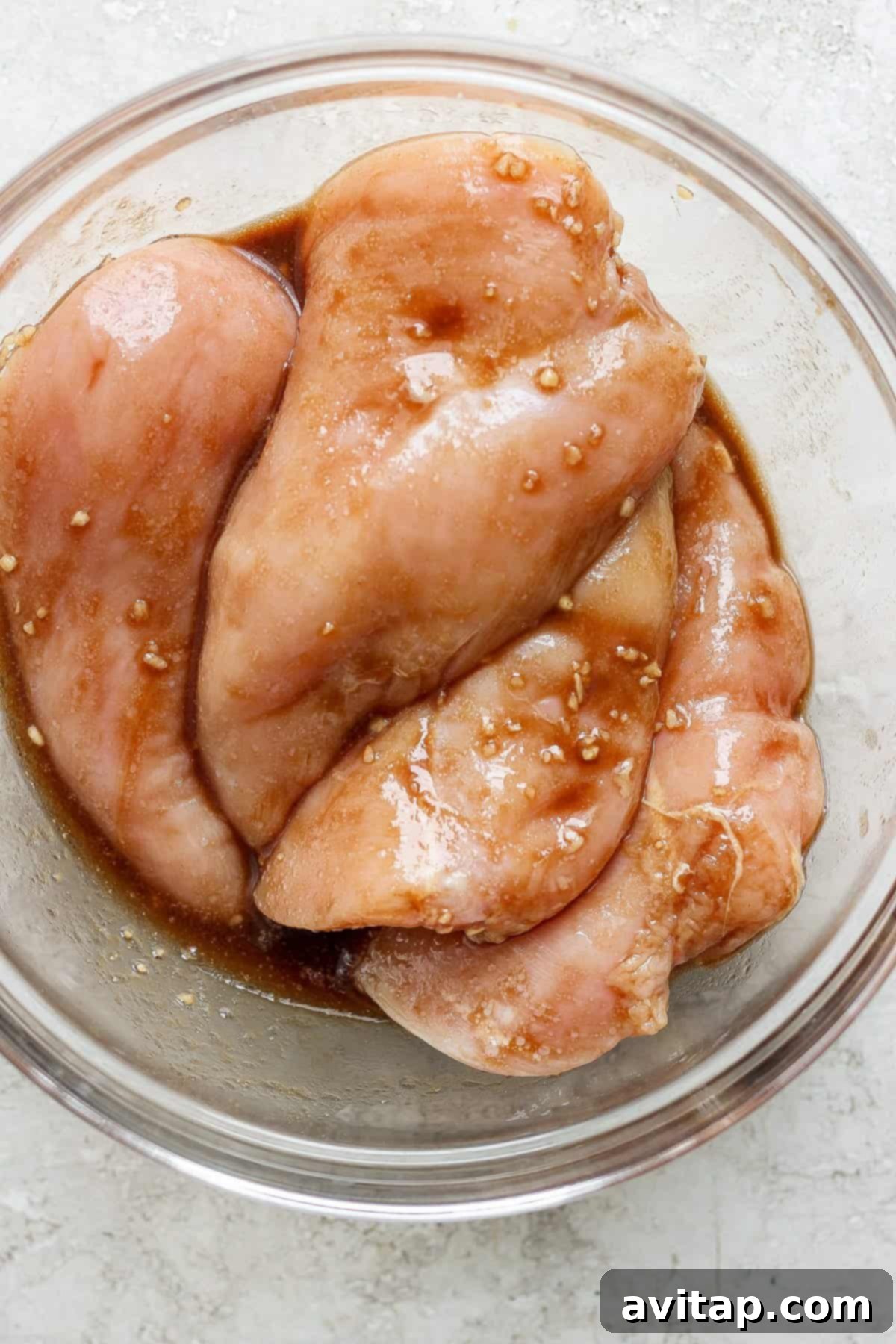 Raw chicken breasts marinating in a seasoned sauce.