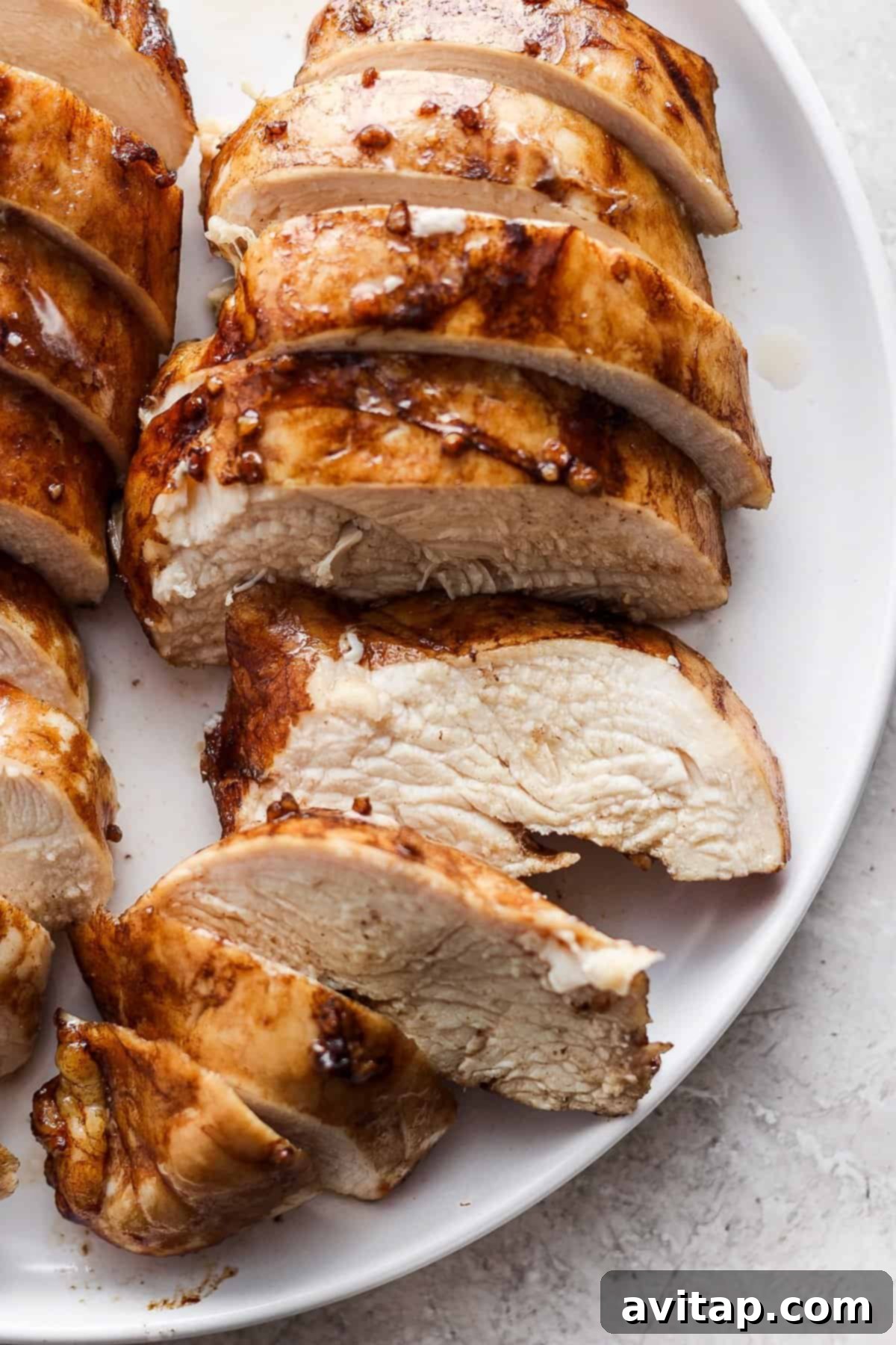 Sliced grilled chicken breast arranged on a white plate, showing juicy interior and golden-brown, seared exterior.