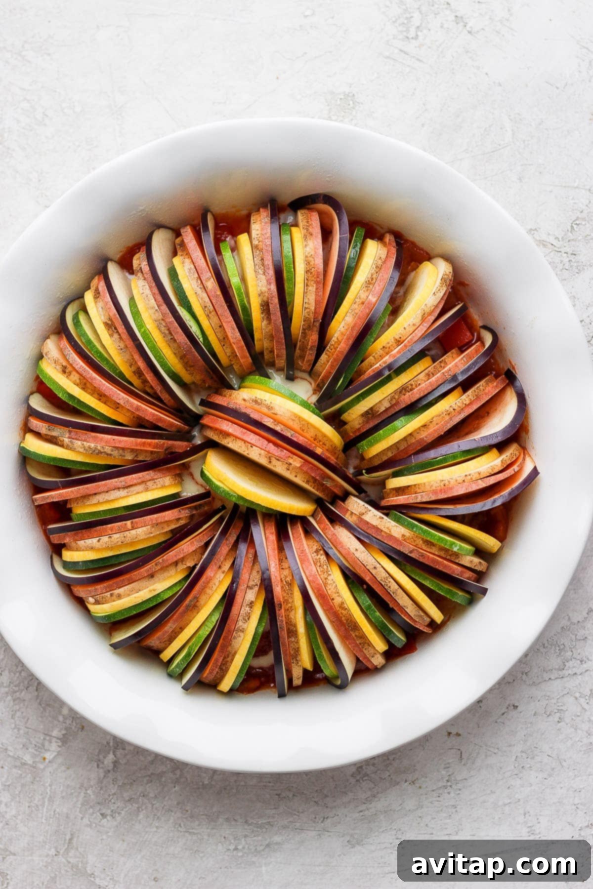 Thinly sliced eggplant, zucchini, and potatoes arranged in a baking dish before adding sauce.