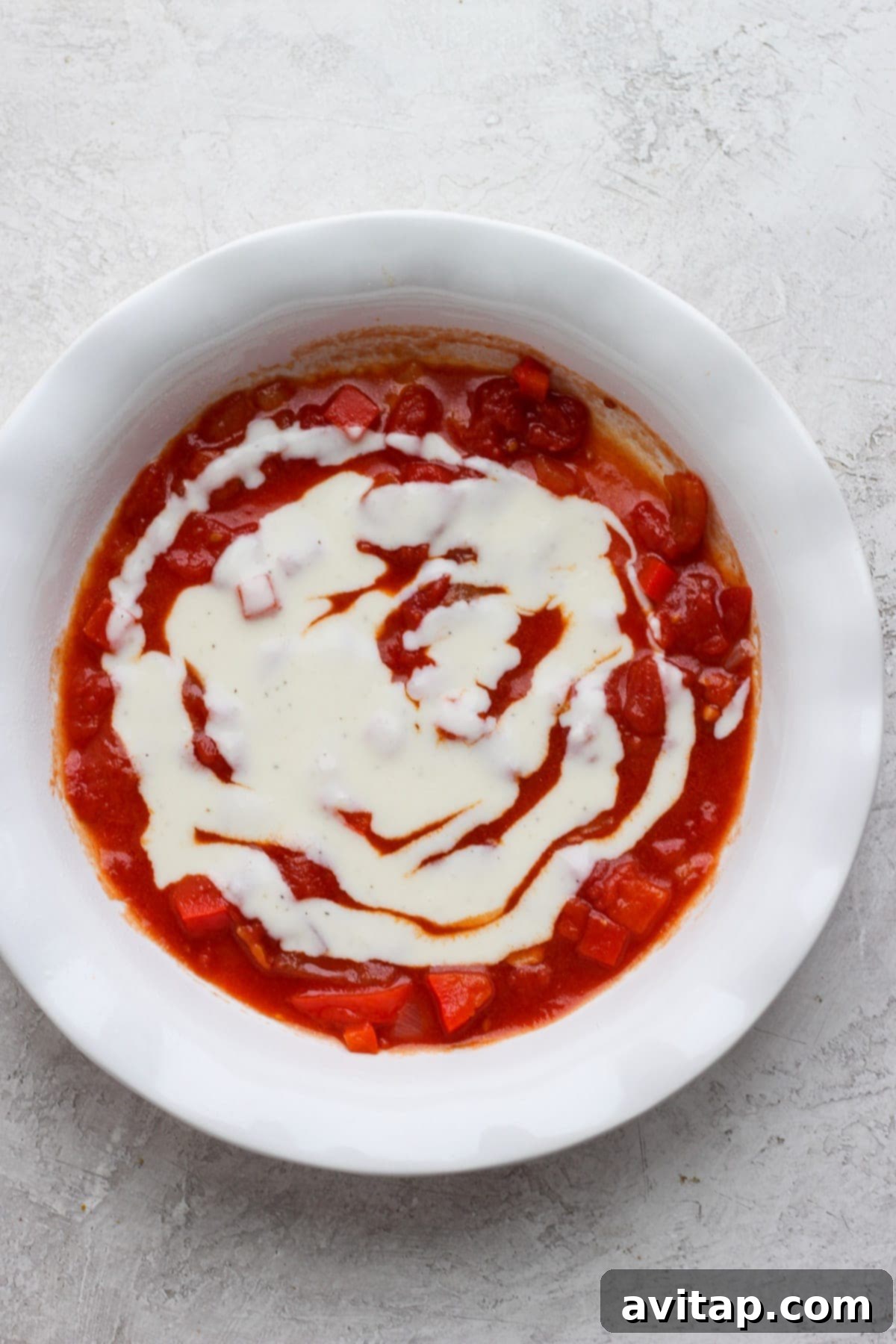 Red tomato sauce and white béchamel sauce spread evenly in the bottom of a baking dish.