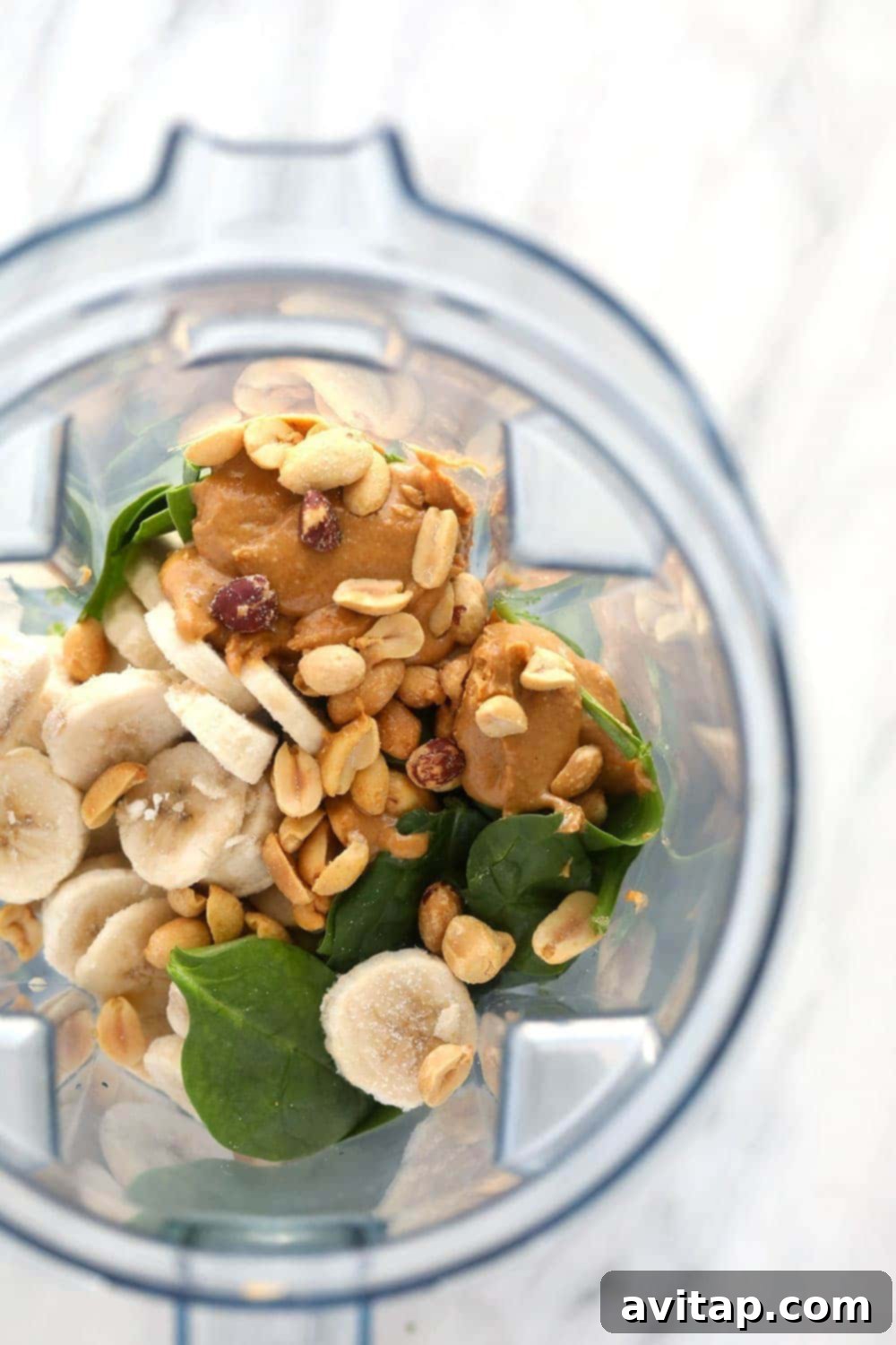 Have fun with your green smoothie recipe and add your favorite ingredients such as peanuts, peanut butter, and banana! A blender filled with ingredients for a green smoothie, showcasing its potential for customization.