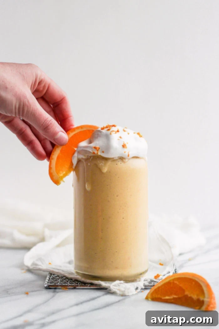 Delicious Orange Creamsicle Smoothie Vibrant orange creamsicle smoothie in a glass, with a hand reaching for a fresh orange slice
