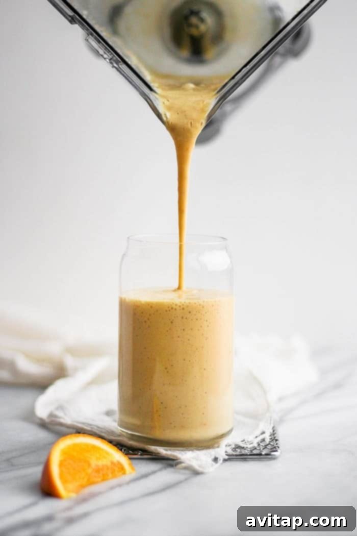 Pouring the Refreshing Orange Creamsicle Smoothie Preparing the orange creamsicle smoothie, pouring the blended mixture into a tall glass with a vibrant orange color.