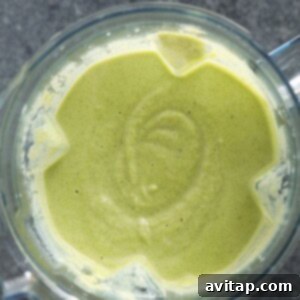 A green liquid, the blended broccoli cauliflower cheese soup, in a high-speed blender.