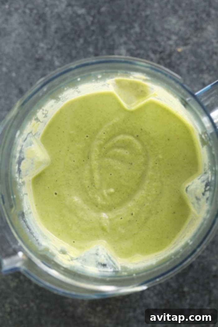 A green liquid, the broccoli cauliflower cheese soup, in a high-speed blender, showing its smooth consistency.