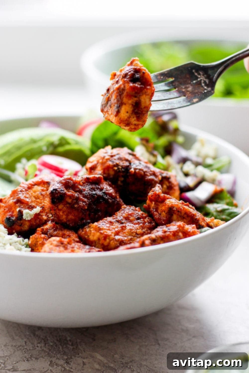 A fork holding a piece of crispy sriracha chicken, highlighting its texture and glaze.