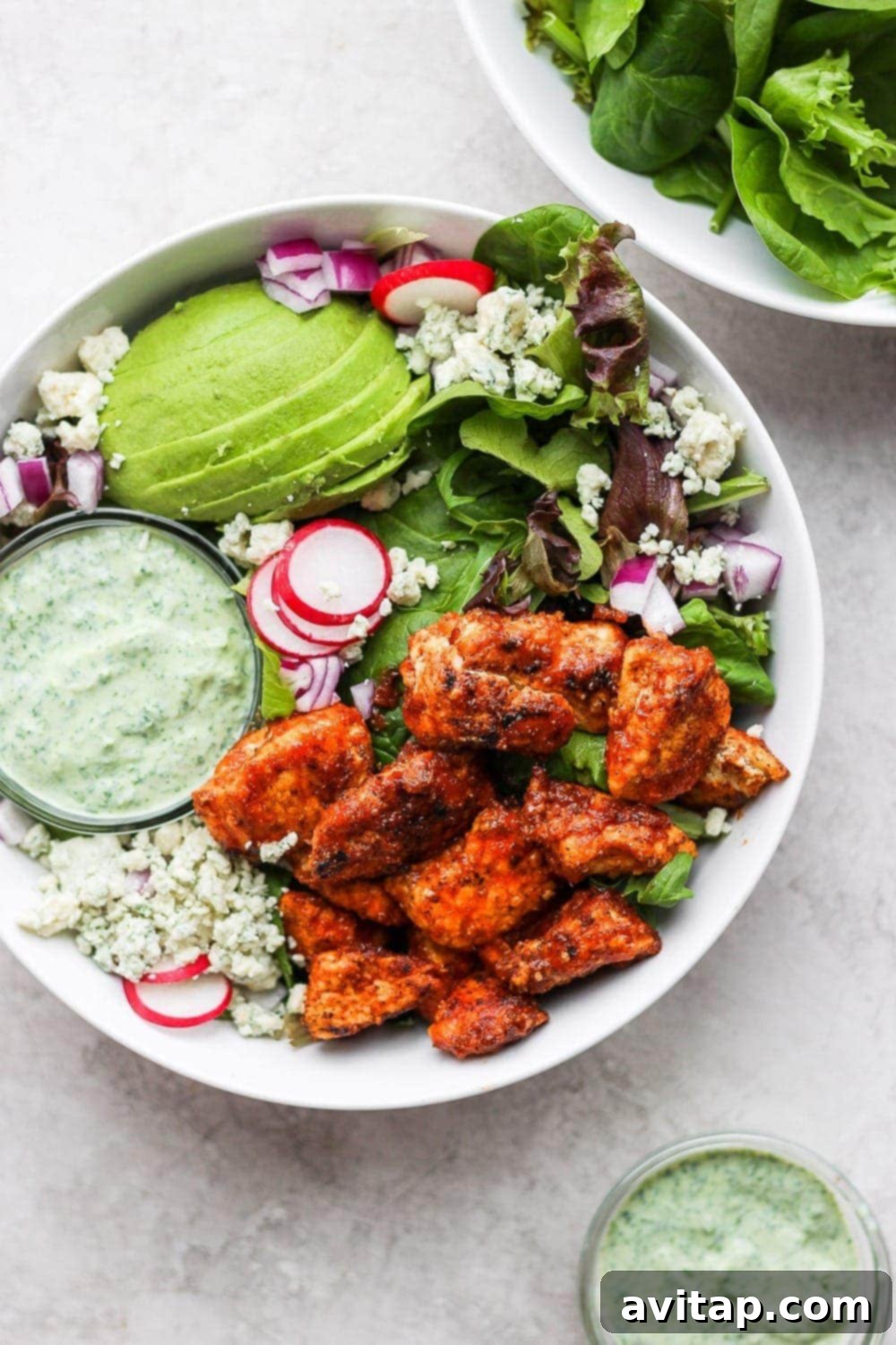 A vibrant Sriracha Chicken Salad, beautifully plated with creamy avocado, radishes, and blue cheese crumbles.