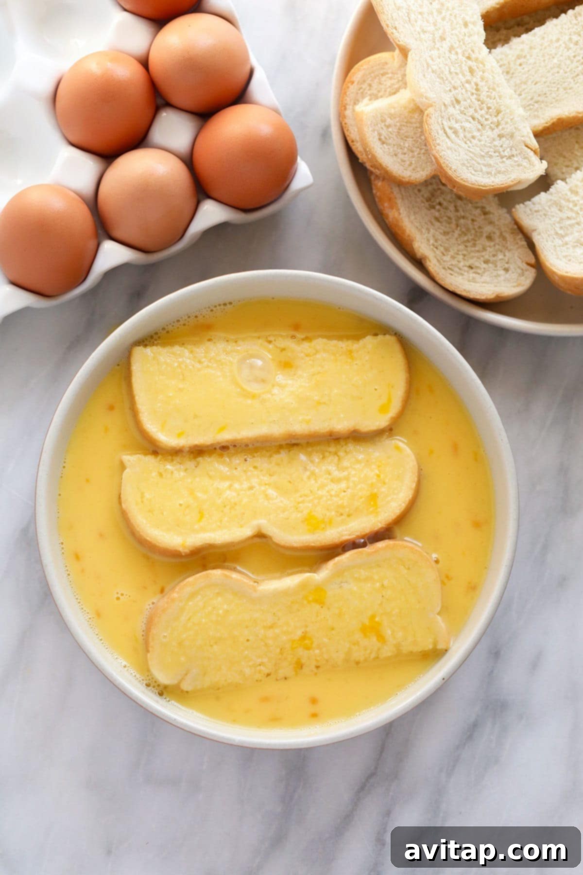 Soaking Bread for French Toast Sticks Batter Absorption Thick-cut bread slices being carefully dipped and thoroughly soaked in the rich egg mixture for French Toast Sticks.
