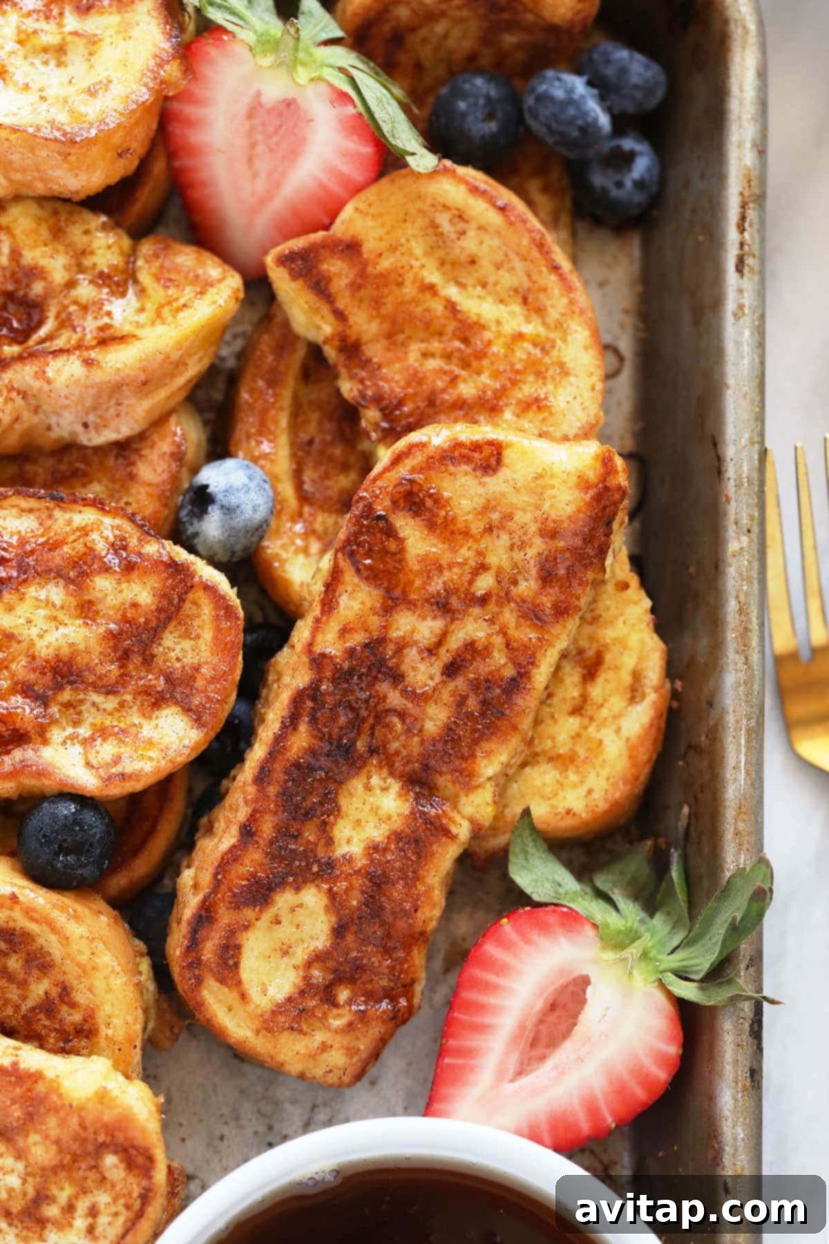 French Toast Sticks Served with Fresh Strawberries A beautifully arranged platter of golden French Toast Sticks, elegantly garnished with fresh, ripe strawberries, presented on a sturdy baking sheet.