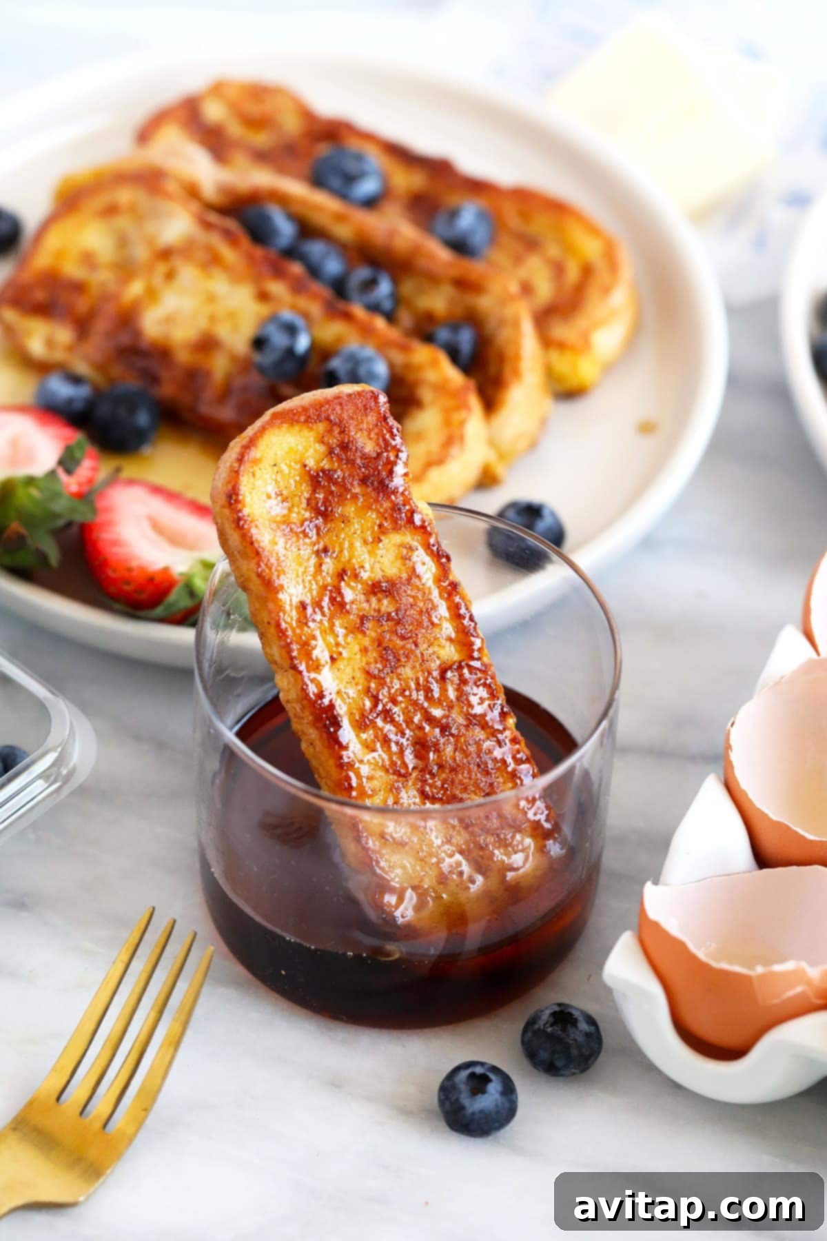 French Toast Stick with Maple Syrup Dip A single golden French toast stick perfectly dipped into a small cup brimming with rich, golden maple syrup, ready to be enjoyed.