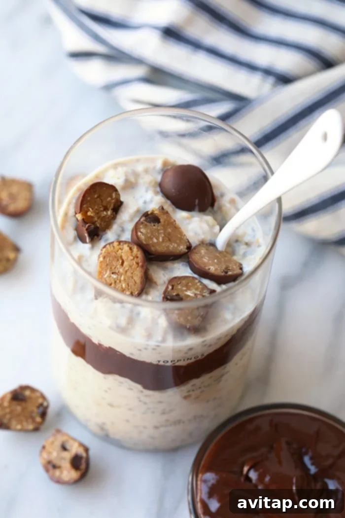 Close-up of creamy overnight oatmeal generously topped with visible cookie dough chunks and a rich fudge swirl.
