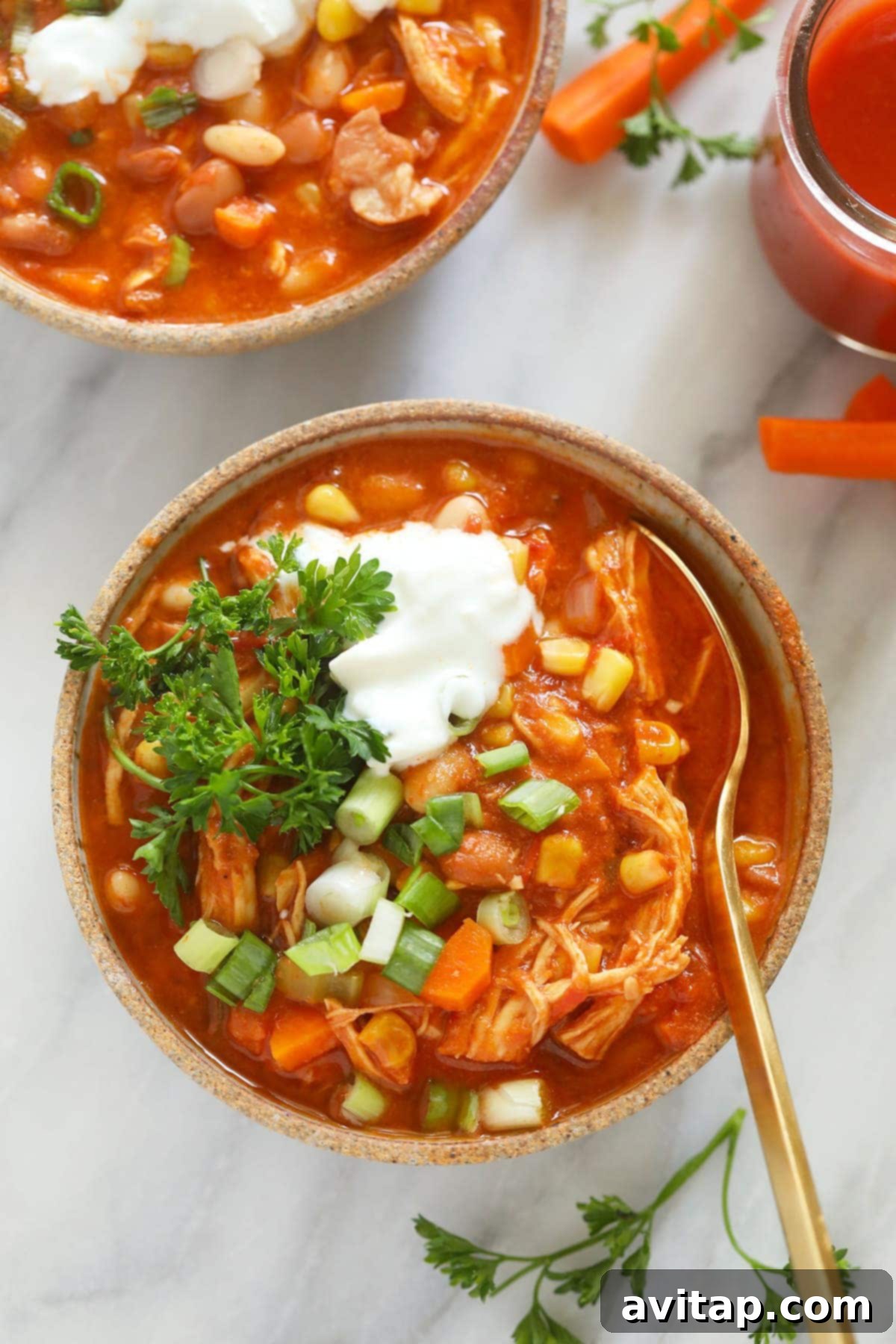 A steaming bowl of Instant Pot Buffalo Chicken Chili, garnished with fresh herbs and a drizzle of dressing, with a spoon ready for tasting.