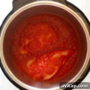 Crushed tomatoes, buffalo sauce, and spices added to the Instant Pot with chicken breasts submerged.