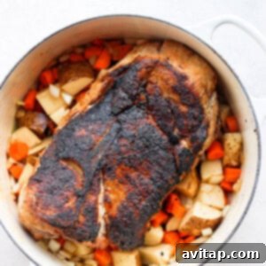 Pork shoulder meticulously placed on a colorful bed of raw potatoes, carrots, and onions in a stockpot, prepared for the braising liquid.