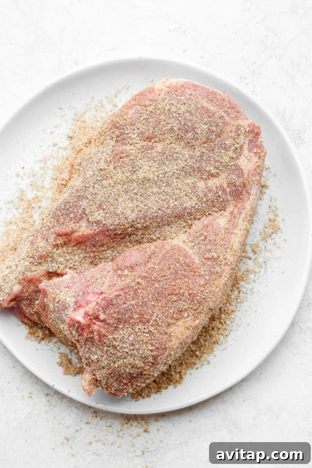 Achieve the perfect crispy crust and tender interior with our aromatic dry-rubbed pork roast recipe. Pork shoulder generously patted with a vibrant, reddish-brown dry rub, showcasing rich seasoning and texture.