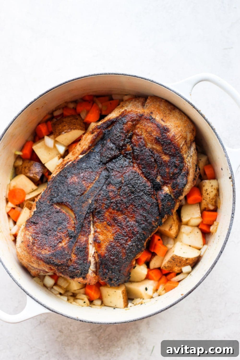 Prepare your pork roast with vibrant, chunky vegetables for a deeply flavorful and wholesome oven-baked meal. Flavorfully dry-rubbed pork shoulder placed on a generous bed of chopped potatoes, carrots, and onions in a roasting pan, perfectly arranged and ready for the oven to begin the roasting process.