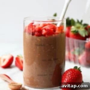 A glass jar filled with rich chocolate overnight oats, topped generously with sliced fresh strawberries and a spoon ready for enjoyment.