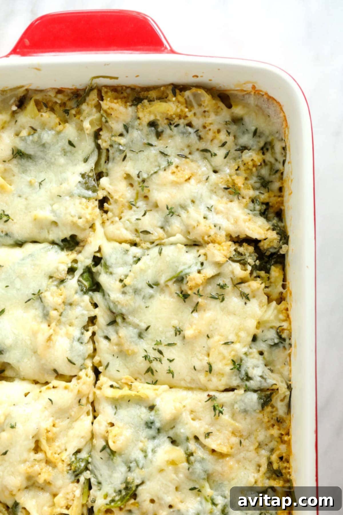 Baked spinach artichoke quinoa casserole with melted cheese on top, garnished with fresh herbs.