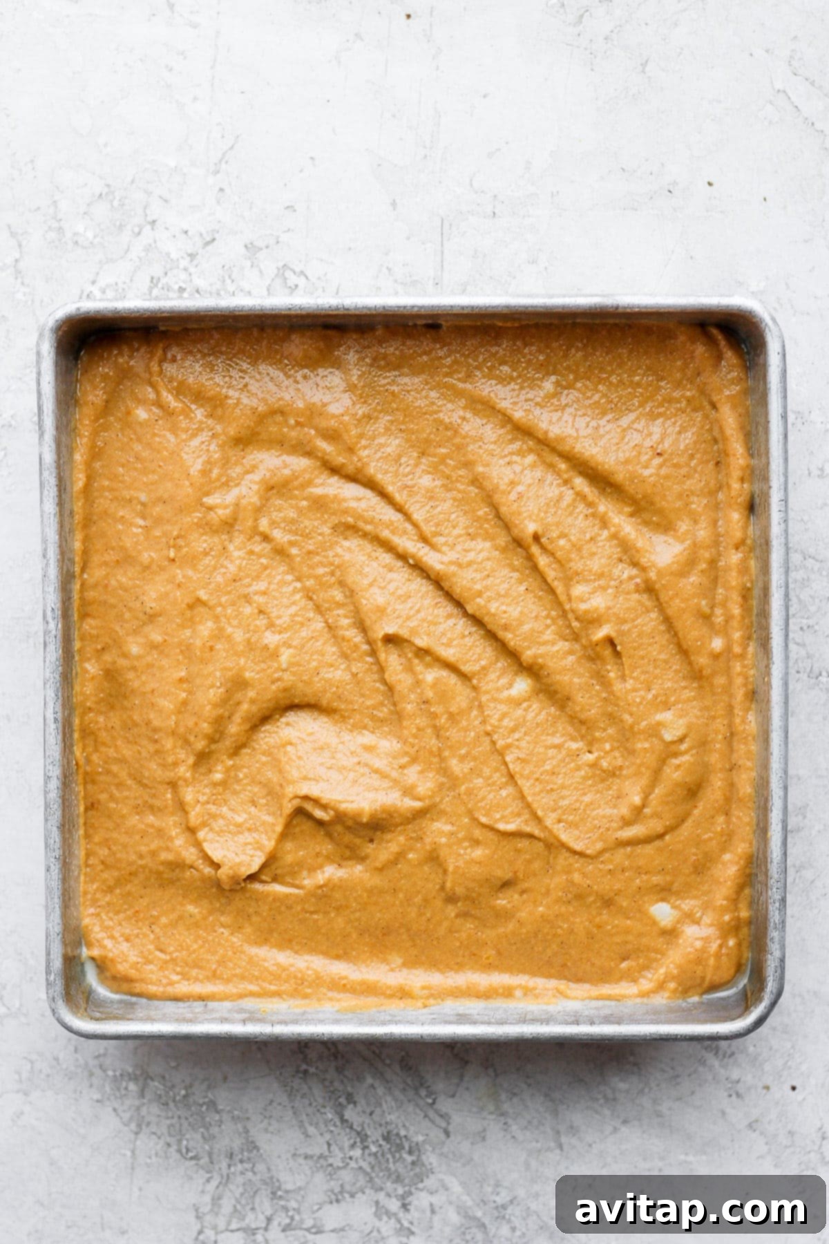 Smooth pumpkin sheet cake batter filling a square baking pan, ready for the oven.