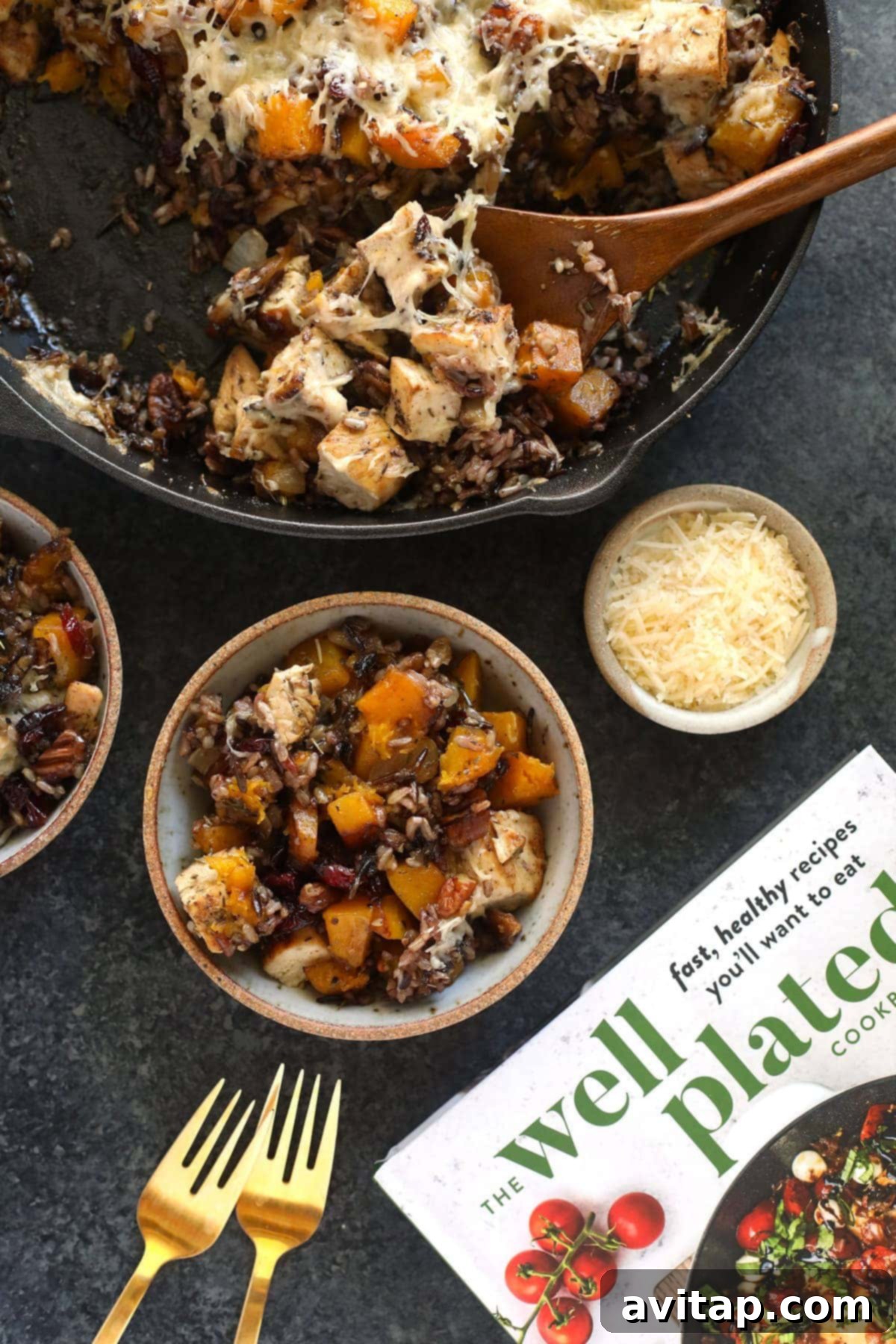 Butternut squash wild rice casserole being scooped from a cast iron pan with a wooden spoon, ready to serve.