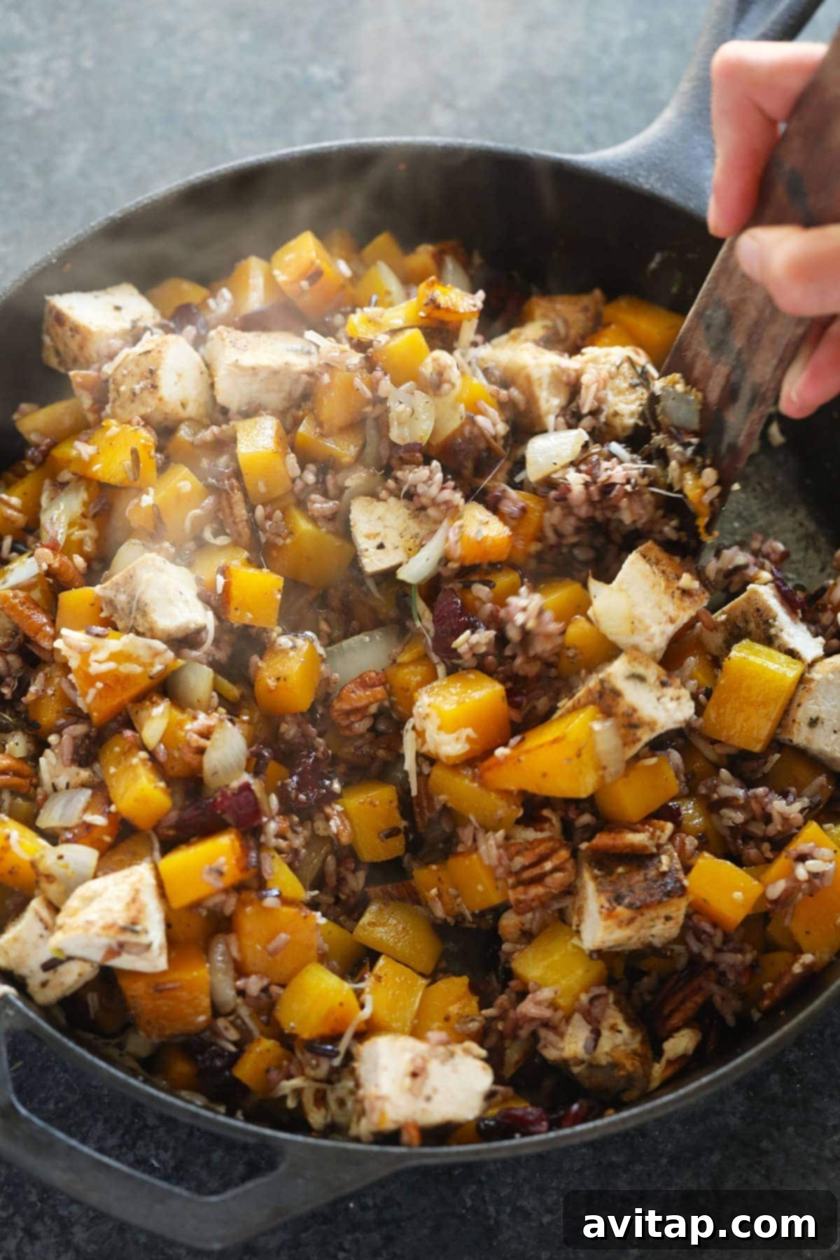 Butternut squash wild rice casserole ingredients being mixed together in a large cast iron pan before baking.