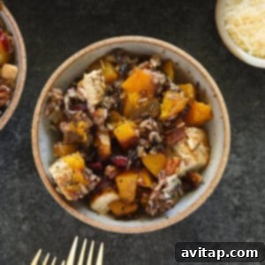 Two bowls of butternut squash and chicken wild rice casserole with a fork on a table, garnished with fresh herbs.