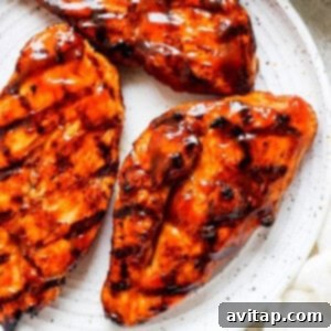 Grilled chicken breasts served on a white plate with extra BBQ sauce.